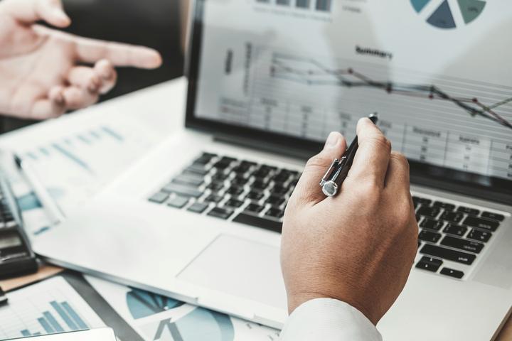 グラフを表示したノートPCを指し示す手元